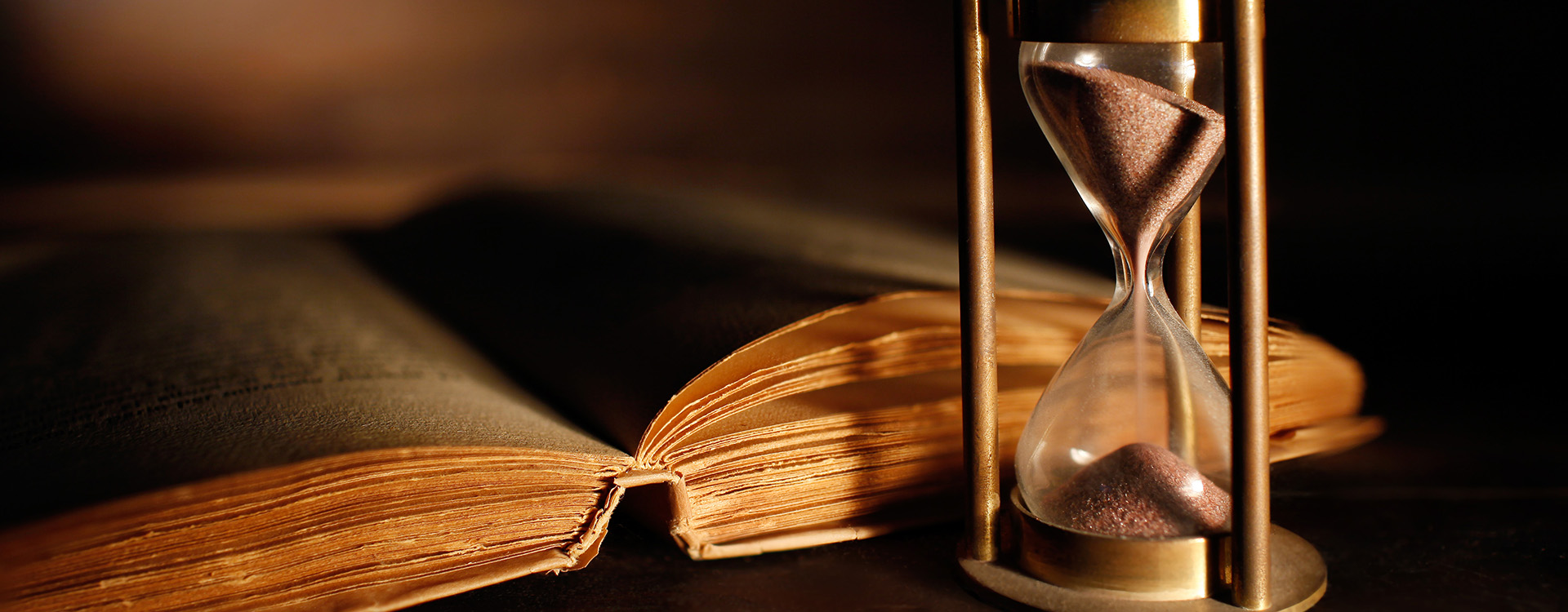 Old book on wooden desk with sand timer